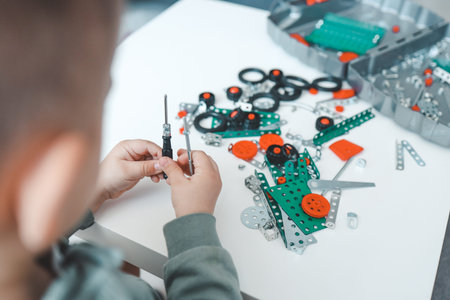 A little boy with a screwdriver in his hands plays with a metal constructor.