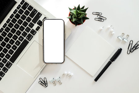 Top view of minimal workspace with blank screen smartphone, laptop on white color desk