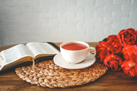 Open bible with tulip flowers and a cup of tea on light wood.の写真素材