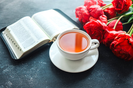 Open book with tulip flowers and a cup of tea on a dark background.