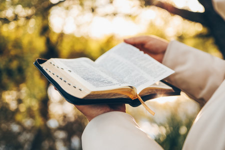 Christian woman holds bible in her hands. Reading the Holy Bible in a field during beautiful sunset....