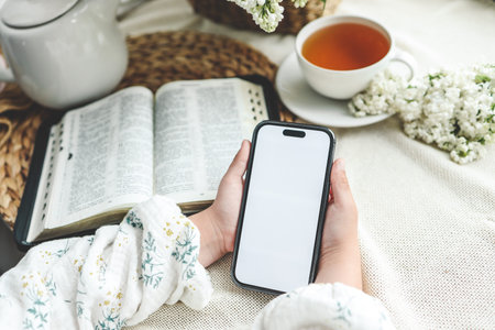 Phone in hands with isolated screen on the background of the bible, space for text.