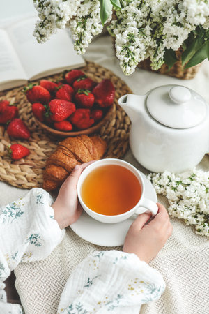 Cup of tea in hands, strawberries and flowers, summer breakfast concept.の写真素材