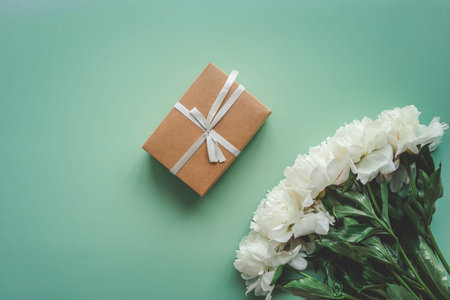 Beautiful white peony flowers on a green background and a gift box with a bow.の写真素材