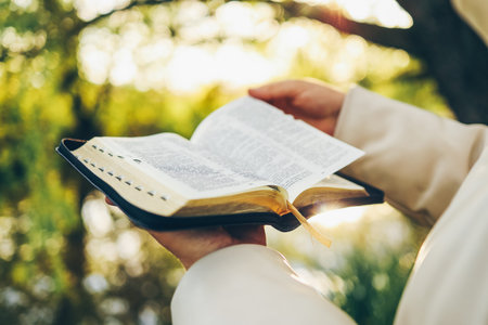 Christian woman holds bible in her hands. Reading the Holy Bible in a field during beautiful sunset....
