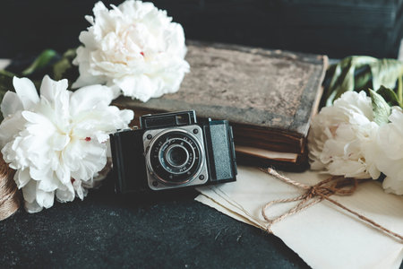 retro photo camera with book and fresh peony flowers.