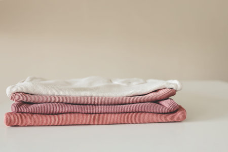 Stack of pink baby clothes on beige background.