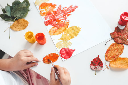 Little girl painting on autumn yellow leaves with gouache, kids arts, children creativity, autumn...