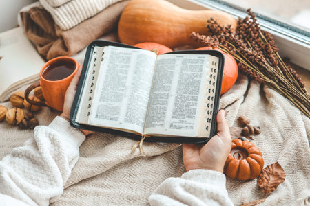 Open Bible in female hands in autumn interior.