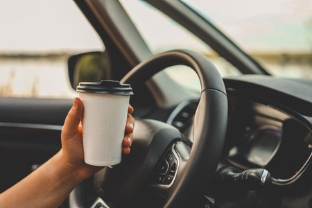 Paper cup with coffee in hand, traveling by car.