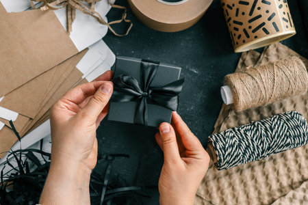 Gift box with a bow in hands on a background of materials for packaging goods and gifts.