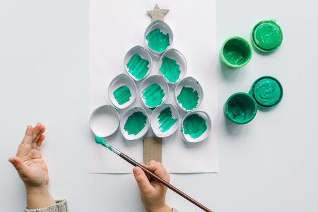 A child draws a Christmas tree. Ideas for drawing with bright colors. Drawing children on a white background. A little girl draws with paint and brushes. The concept of children's development.の写真素材