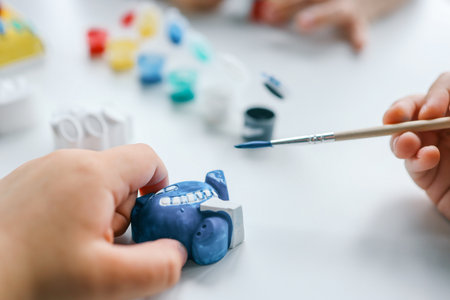 Child paints plaster figure with bright colors. Concept of children's creativity. Preschooler does needlework at home.の写真素材