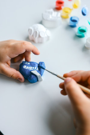 Child paints plaster figure with bright colors. Concept of children's creativity. Preschooler does needlework at home.の写真素材
