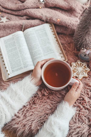 Cup of tea in hands and open Bible, winter morning mood.