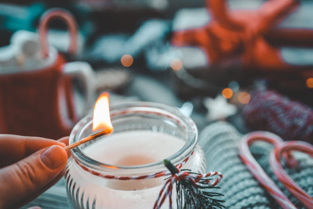 Hand with a match lights a candle, Christmas aesthetics.