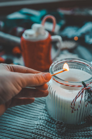 Hand with a match lights a candle, Christmas aesthetics.
