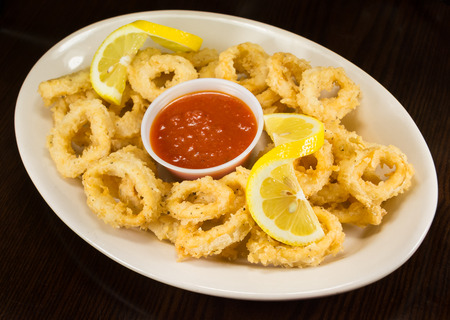 Fried Calamari rings, breaded and deep fried, arranged on a plate with a cup of red tomato marinara sauce and a slice of lemonの写真素材