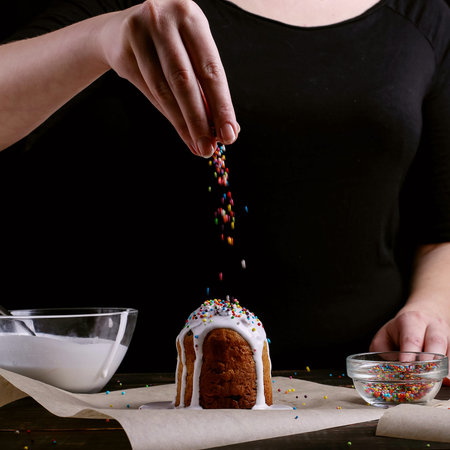 The girl prepares Easter baking, smears the cake with icing and sprinkles with colored powder....