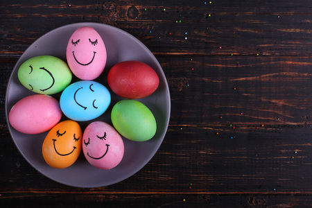 Easter eggs with cute faces on the plate. Preparing for the holiday on the kitchen table, on dark background.の写真素材