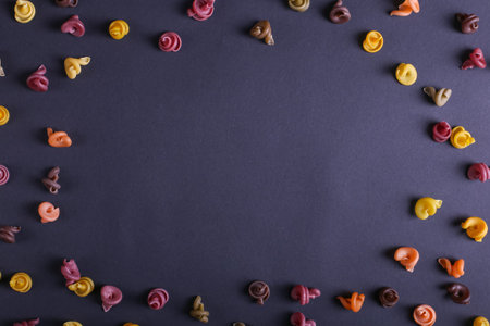 Multicolored pasta with the addition of natural vegetable dye. Scattered on black background, copy...