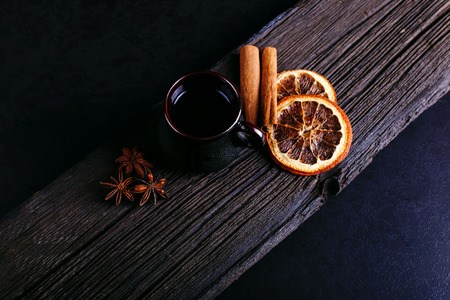 A cup of coffee, star anise, cinnamon, dried orange and coffee beans on a dark kitchen countertop. Fragrant spices for drink, close-up, top view, flat ley.の写真素材