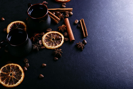 A cup of coffee, star anise, cinnamon, dried orange and coffee beans on a dark kitchen counter top. Fragrant spices for drink, close-up, top view.の写真素材
