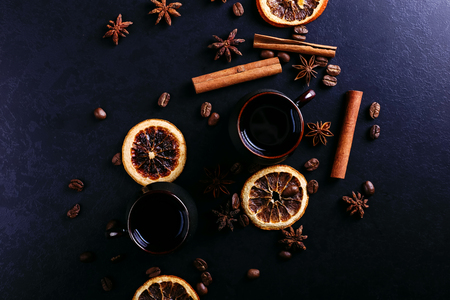 A cup of coffee, star anise, cinnamon, dried orange and coffee beans on a dark kitchen countertop. Fragrant spices for drink, close-up, top view, flat ley.の写真素材