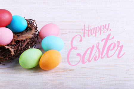 Colored Easter eggs in nest, on a white wooden table.の写真素材