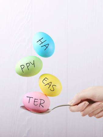 Female hand holds a spoon on which multi-colored eggs are balanced, on white background. Unusual design, Easter concept, copy space.の写真素材