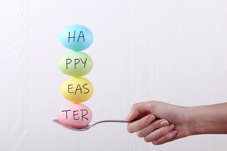 Female hand holds a spoon on which multi-colored eggs are balanced, on white background. Unusual design, Easter concept, copy space.の写真素材