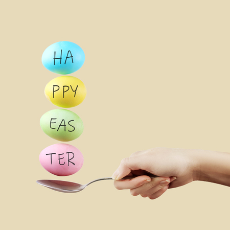 Female hand holds a spoon on which multi-colored eggs are balanced, on yellow background. Unusual design, Easter concept, copy space.の写真素材