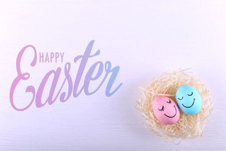 Blue and pink eggs with painted smiles in the nest, copy space. Happy Easter concept, greeting card design.の写真素材
