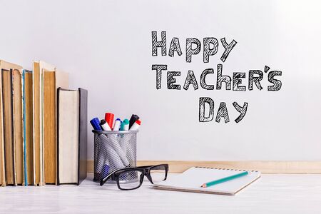 The inscription marker on a white board, Happy Teachers Day. A table with books, glasses and attributes for writing.の写真素材