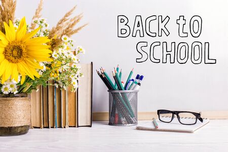 The inscription marker on a white board, Back to School. A table with books, a bouquet of flowers, glasses and attributes for writing.の写真素材