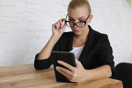 The girl sits at a table with a tablet, in a jacket and glasses. Comfortably work at home remotely via video. Copy space.の写真素材