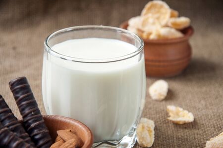 A glass of milk with almond nuts, corn flakes, chocolates, on sacking backgroundの写真素材