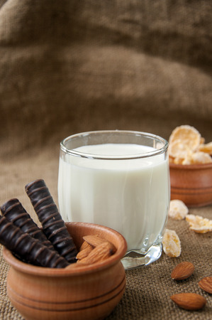 A glass of milk with almond nuts, corn flakes, chocolates, on sacking backgroundの写真素材