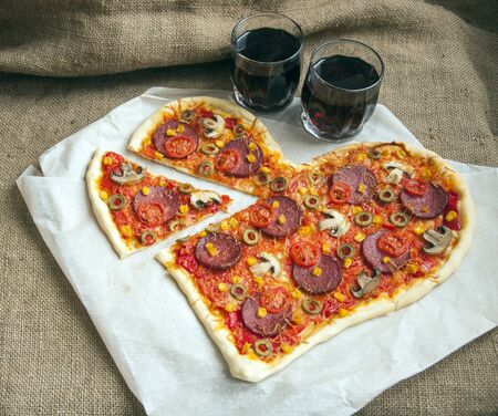 Baked heart-shaped homemade pizza topped with mozzarella and tomato slices, with salami, pepperoni, mushrooms, olives and garlic on parchment paper  close-up. Decorated for Valentine's Dayの写真素材