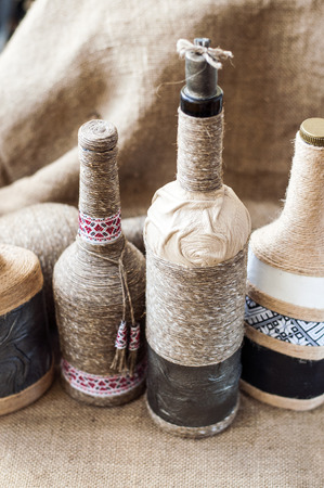 Handmade decorated with twine, cord glass  bottle on the burlap surface and wooden background.の写真素材