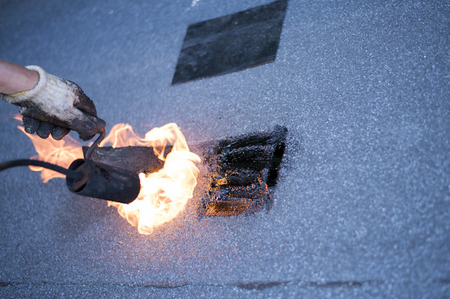 Roofer making repairs waterproofing of the roof, welding patches by using a propane  gas burner and trowel. Installation of roll roofing waterproofing.の写真素材