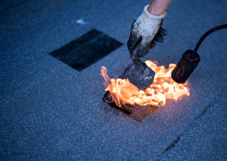 Roofer making repairs waterproofing of the roof, welding patches by using a propane  gas burner and...