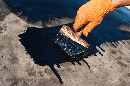Roofer cover the concrete base, polymer modified bitumen waterproofing primer. A worker brushes cover concrete, bitumen-rubber primer.の写真素材
