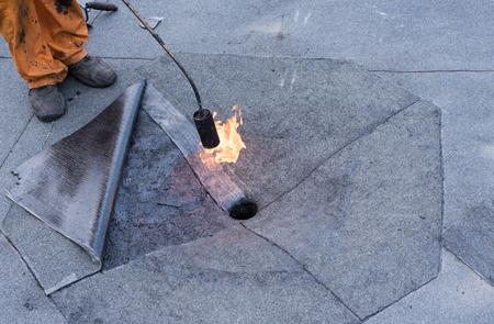 Roofer doing repair  roof drain. Flat roof installation. Heating and melting bitumen roofing felt. Flat roof repairing with roofing felt. Professional master , making waterproofing.の写真素材