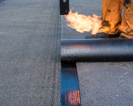 Roofer man worker at building site installing roll of roofing felt with gas blowpipe torch during construction works. flame during welding of a waterproofing membrane on a roofの写真素材