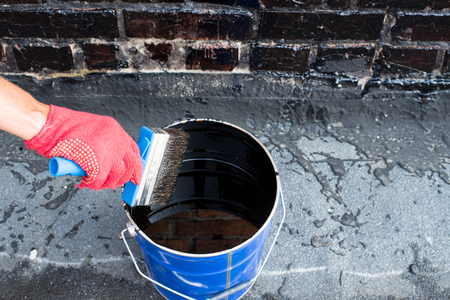 Roofer covered brick wall, bitumen primer for improving adhesion during surfacing, contiguity with rolled waterproofing, during the installation of flat roof.の写真素材