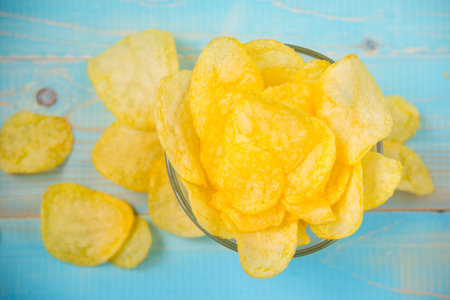 Potato chips in bowl on a blue wooden background
