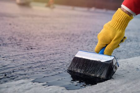 Worker applies bitumen mastic on the foundationの写真素材
