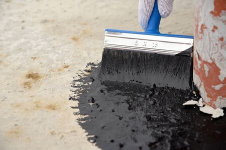 Worker applies bitumen mastic on the foundationの写真素材