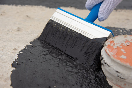Roofer hand with brush closeup. Waterproofing coating. Worker applies bitumen mastic on the...